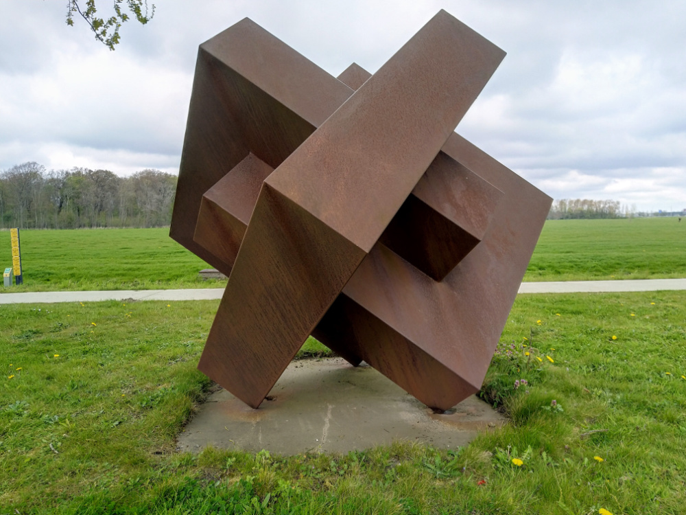Het geometrische stalen kunstwerk Kubus van Truce Wilmink, in een groen landschap in Heiloo
